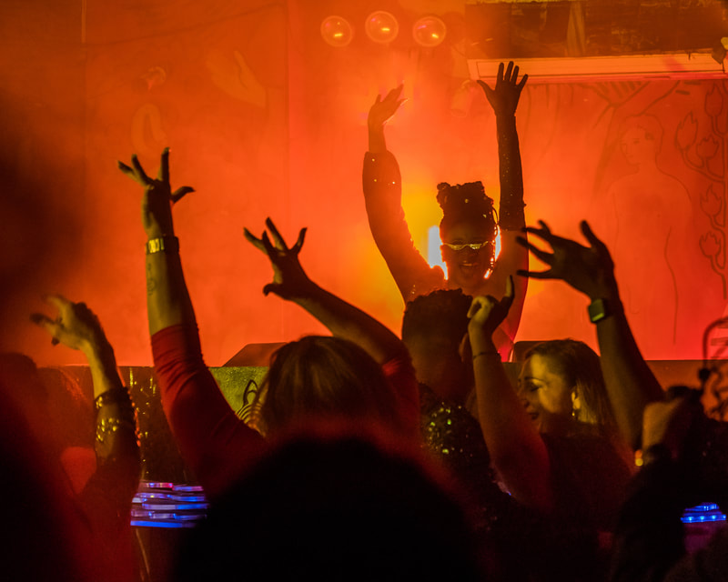 Lachi has her hands raised DJing at a full club in red light